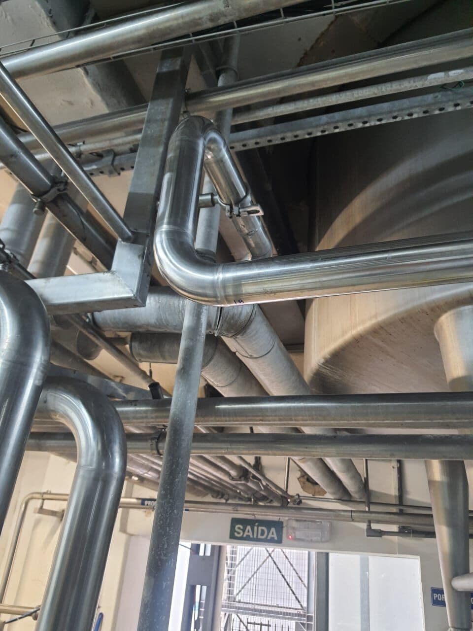 Tubulação industrial correndo sobre suportes no teto da planta