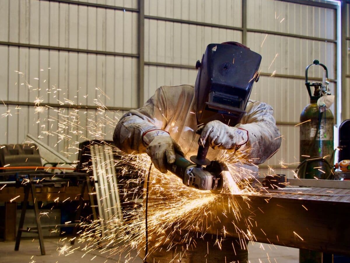 Esmerilhamento de peça metálica em galpão de fabricação