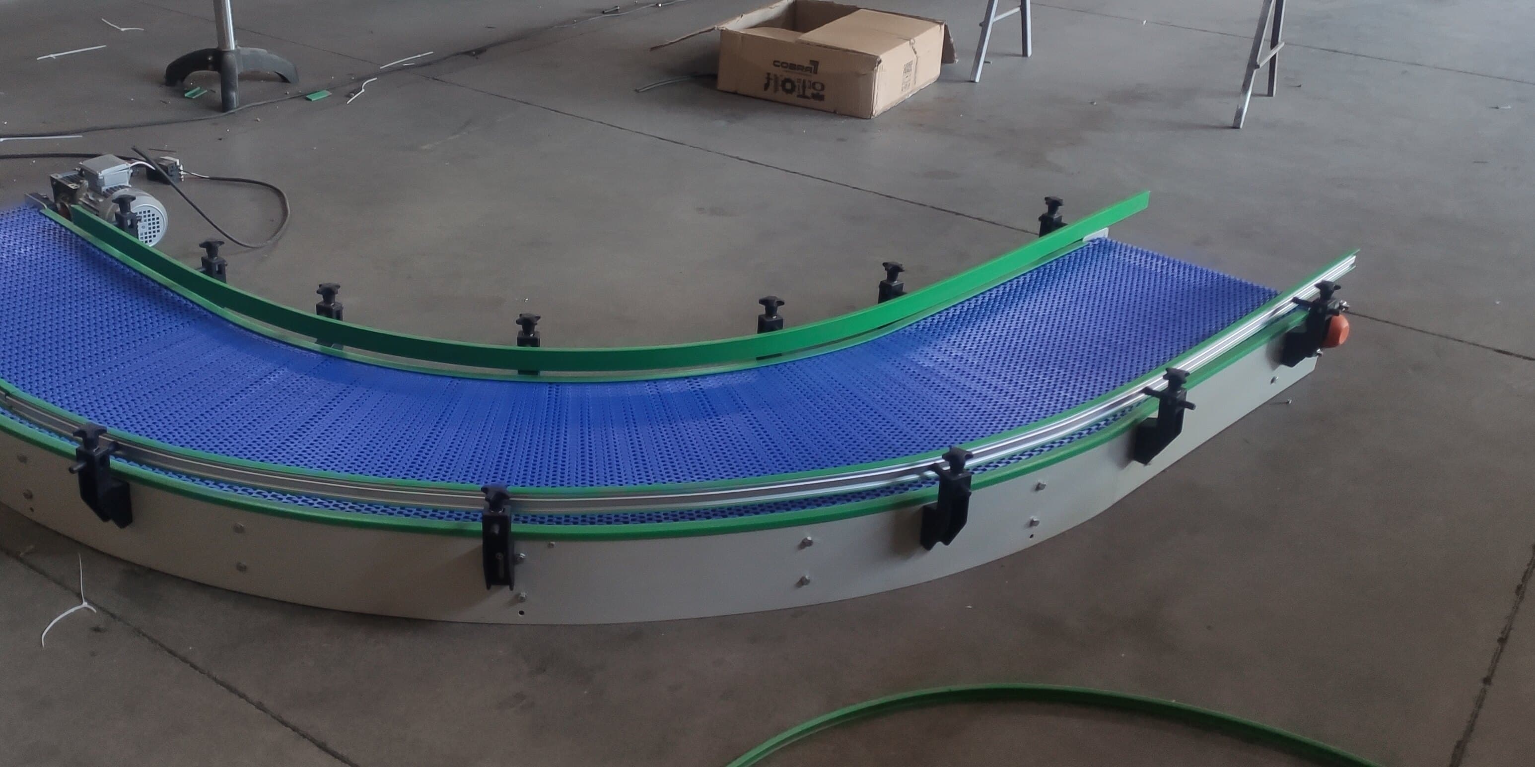 Esteira modular azul em curva, com guias laterais, no piso de um galpão