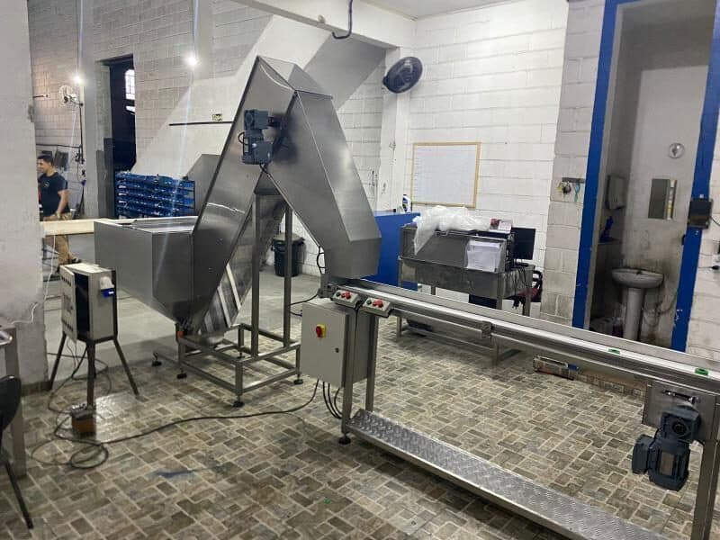 Silo em aço inox com elevador inclinado alimentando uma esteira, na oficina