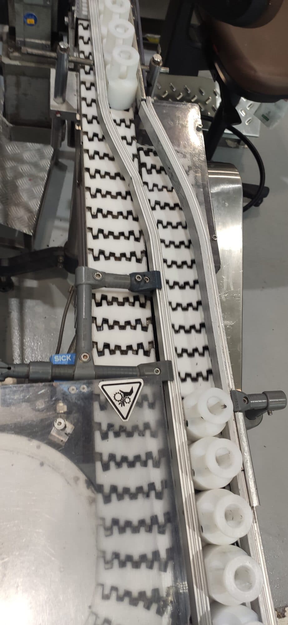 Peças plásticas brancas passando entre duas esteiras modulares, com sensor de presença