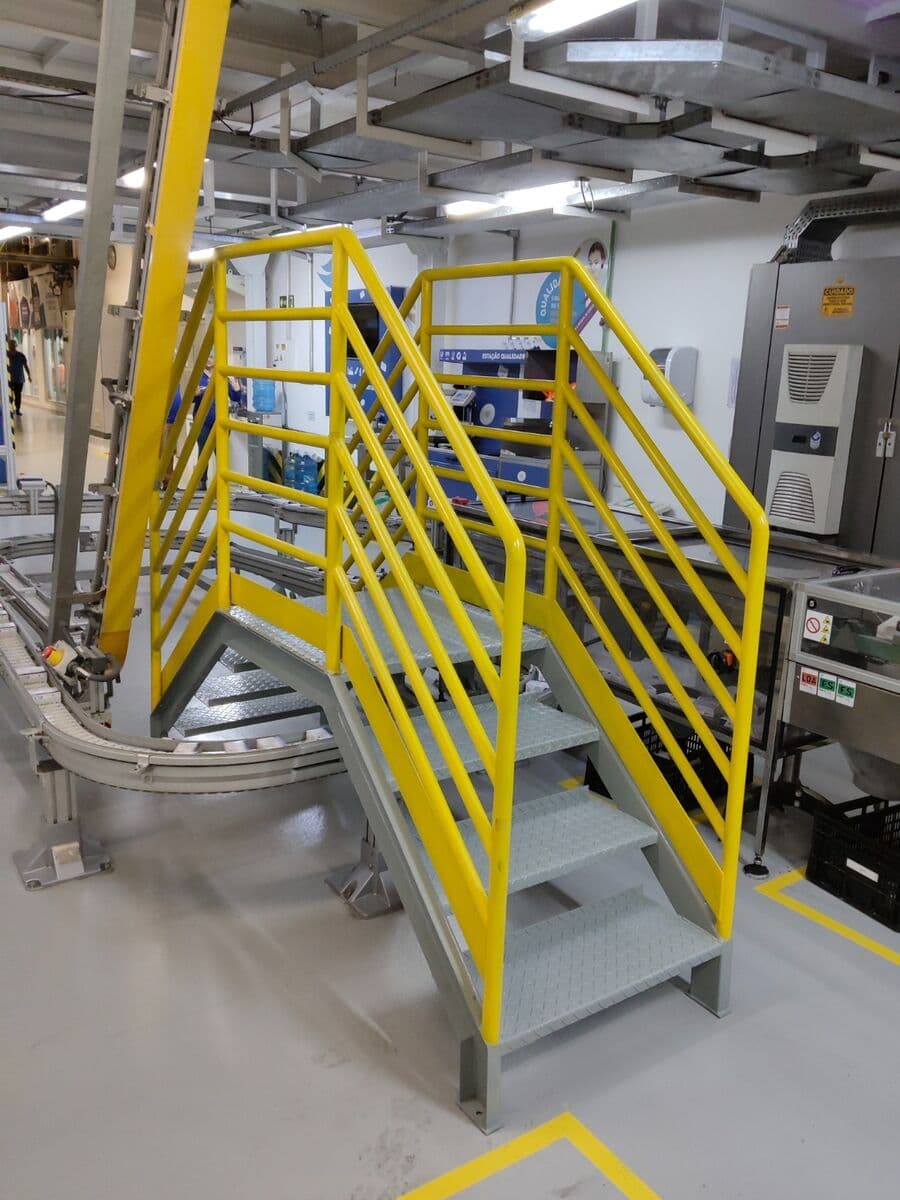 Escada e plataforma de acesso com guarda-corpo sobre uma linha de produção